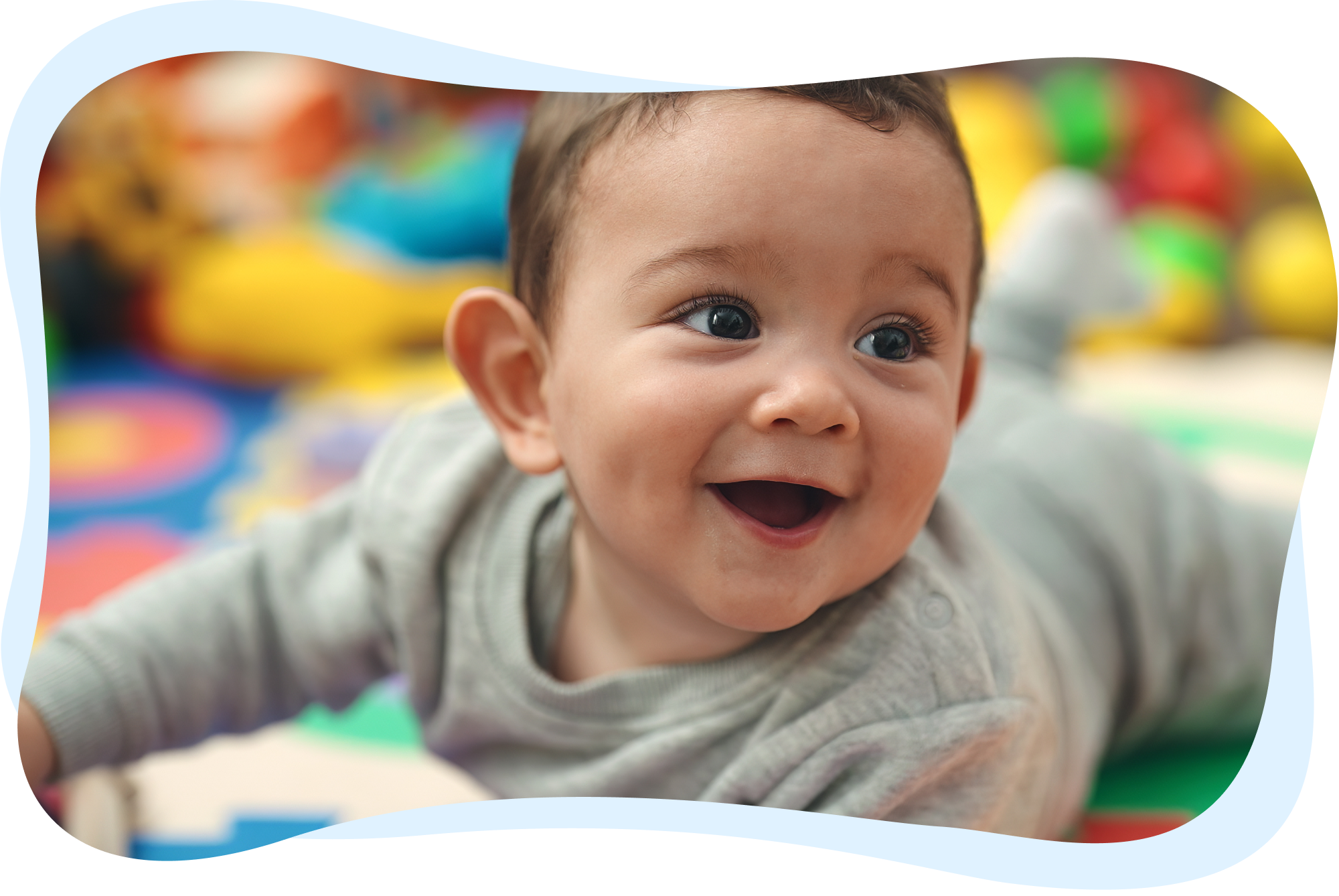 A close-up of a smiling baby lying on a colorful play mat.