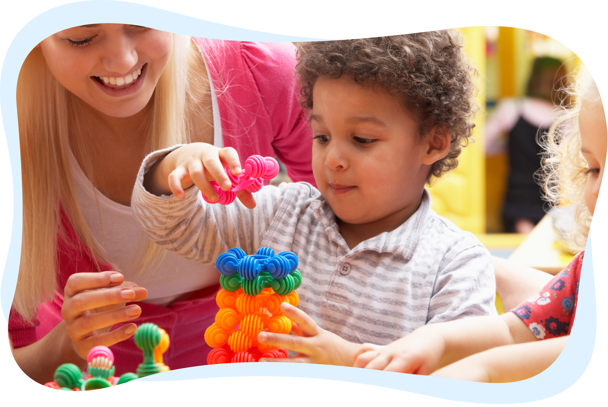 A young boy concentrating on building a structure with colorful interlocking toys, guided by an adult.