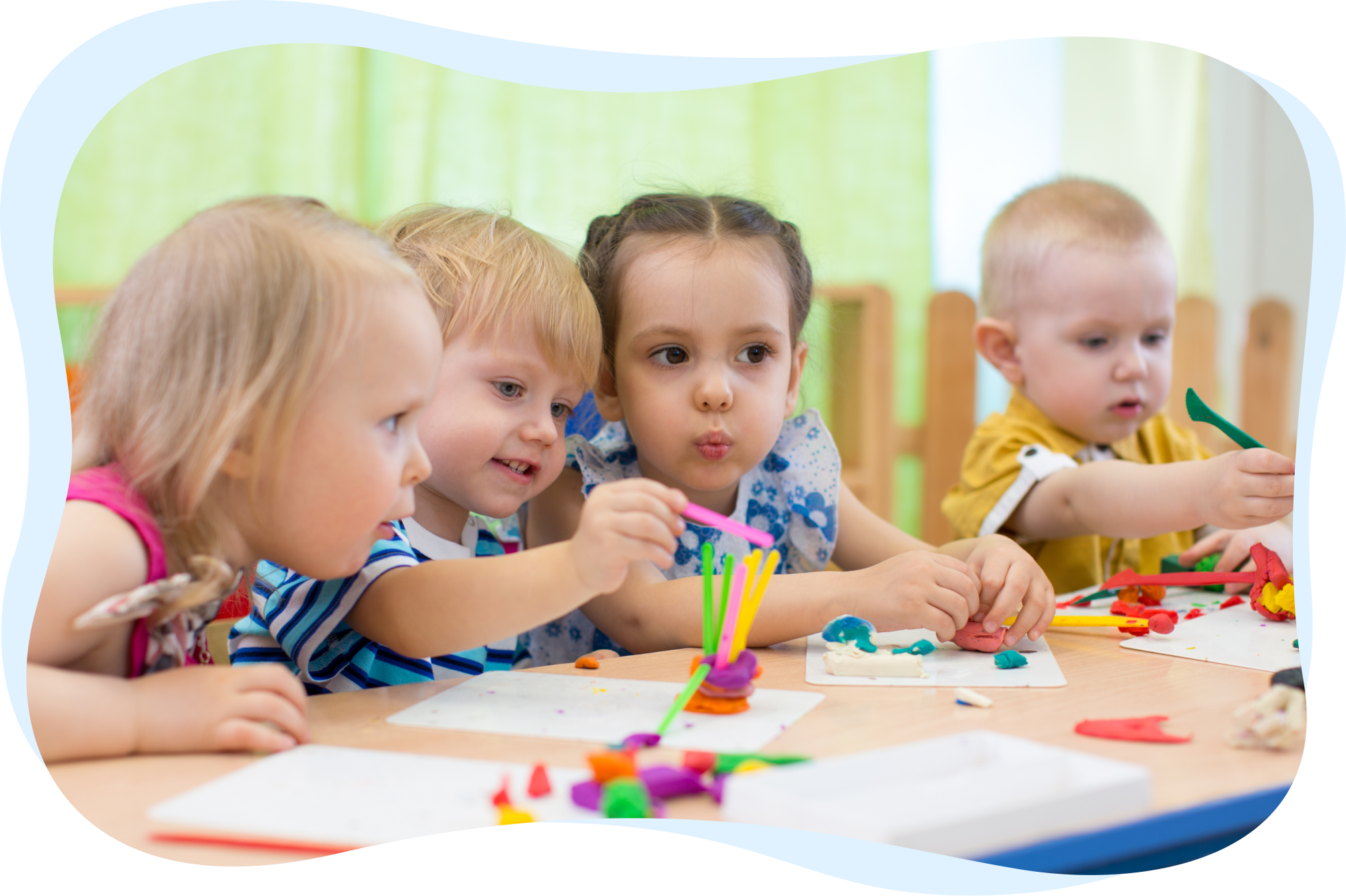 Four young children sitting at a table, engaged in a colorful craft activity with playdough and sticks.