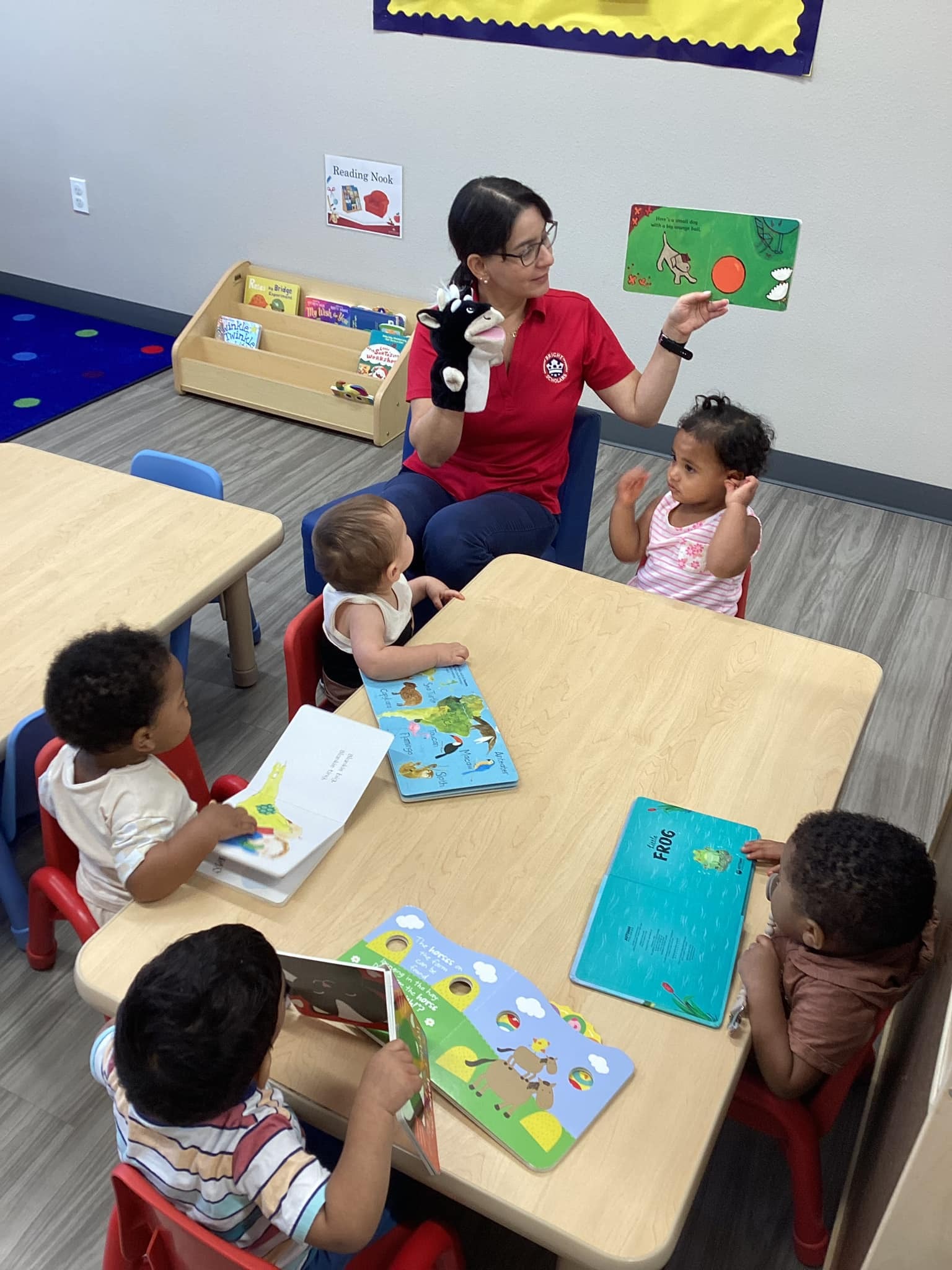 A teacher reads a book to young children at a small table, using a cow puppet to engage them during storytime at Bright Scholars.